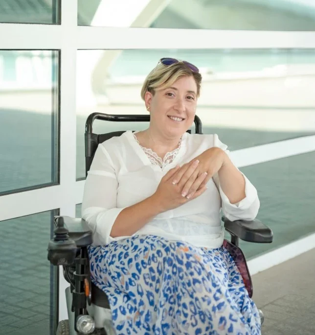 Woman in wheelchair with palms clasped smiling at camera